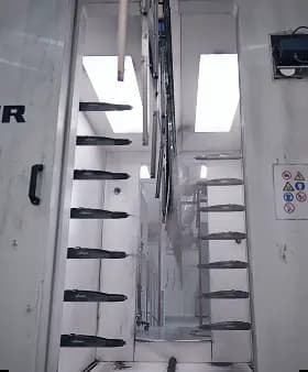 Interior view of an automated powder coating spray booth with nozzle rows preparing components for painting